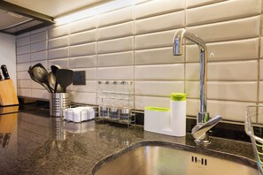A kitchen with a stainless steel sink, a knife block, a utensil holder, and a glass container.