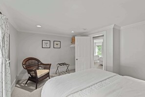 Een slaapkamer met een bed, een stoel, een deur en twee foto's in lijsten aan de muur.
