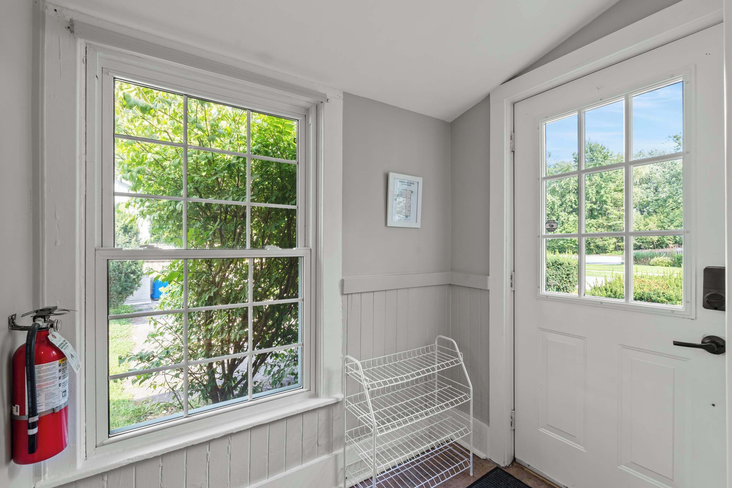 A room with two large windows, a white door, and a fire extinguisher mounted on the wall.