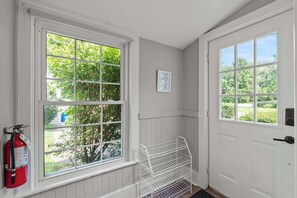 Een kamer met twee grote ramen, een witte deur en een brandblusser aan de muur.