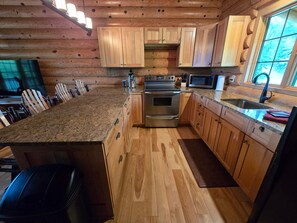 A kitchen with wooden cabinets, a granite countertop, stainless steel appliances, and a window with a view.