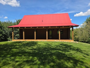 Une cabane en rondins avec un toit rouge, entourée d’une pelouse bien entretenue et d’arbres.
