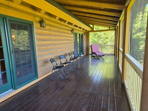 Une véranda couverte avec un plancher en bois, une rangée de chaises et une seule chaise rose.