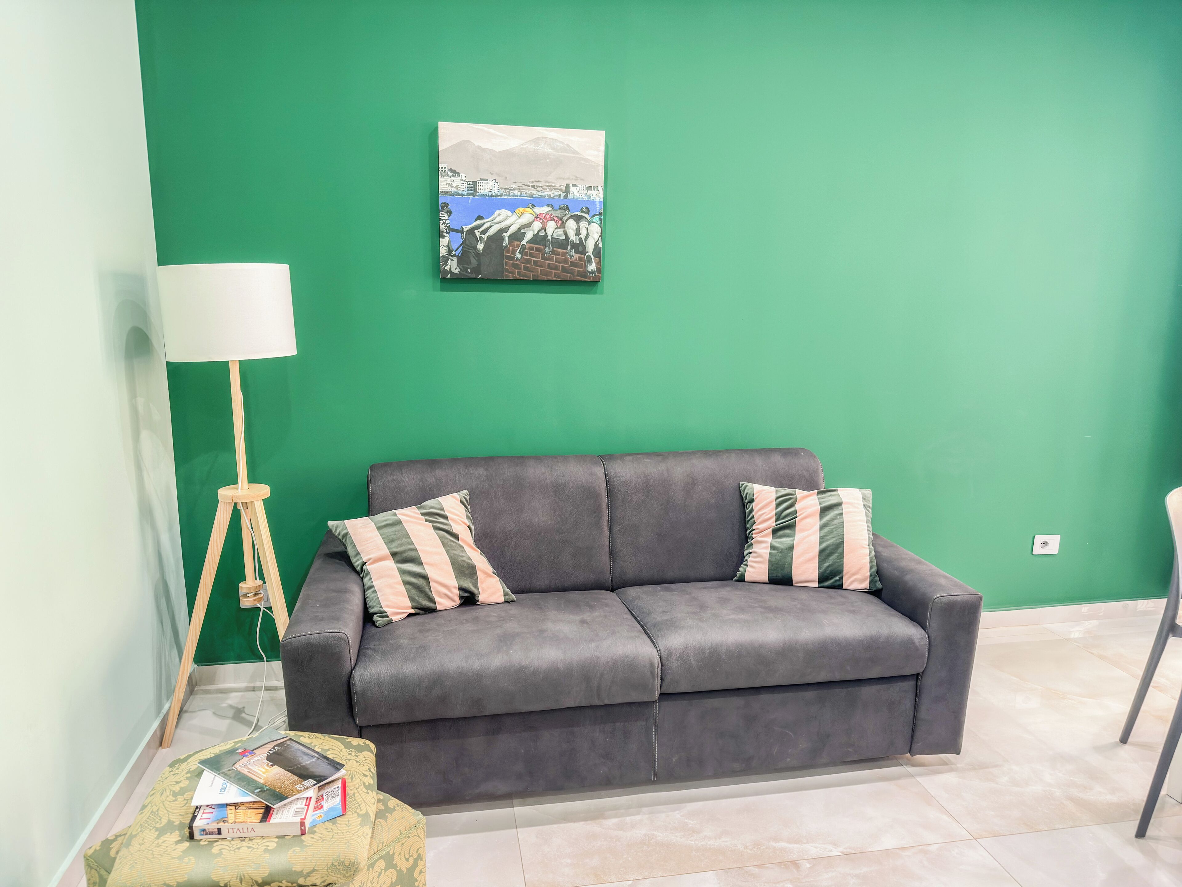 A room with a grey sofa, two striped pillows, a floor lamp, and a small table with books.