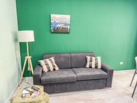 Una habitación con un sofá gris, dos almohadas a rayas, una lámpara de pie y una mesita con libros.