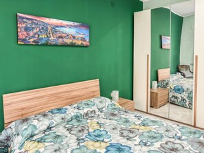 A bedroom with a bed, a nightstand, a mirror, and a green wall. - Karim's House (Portici)