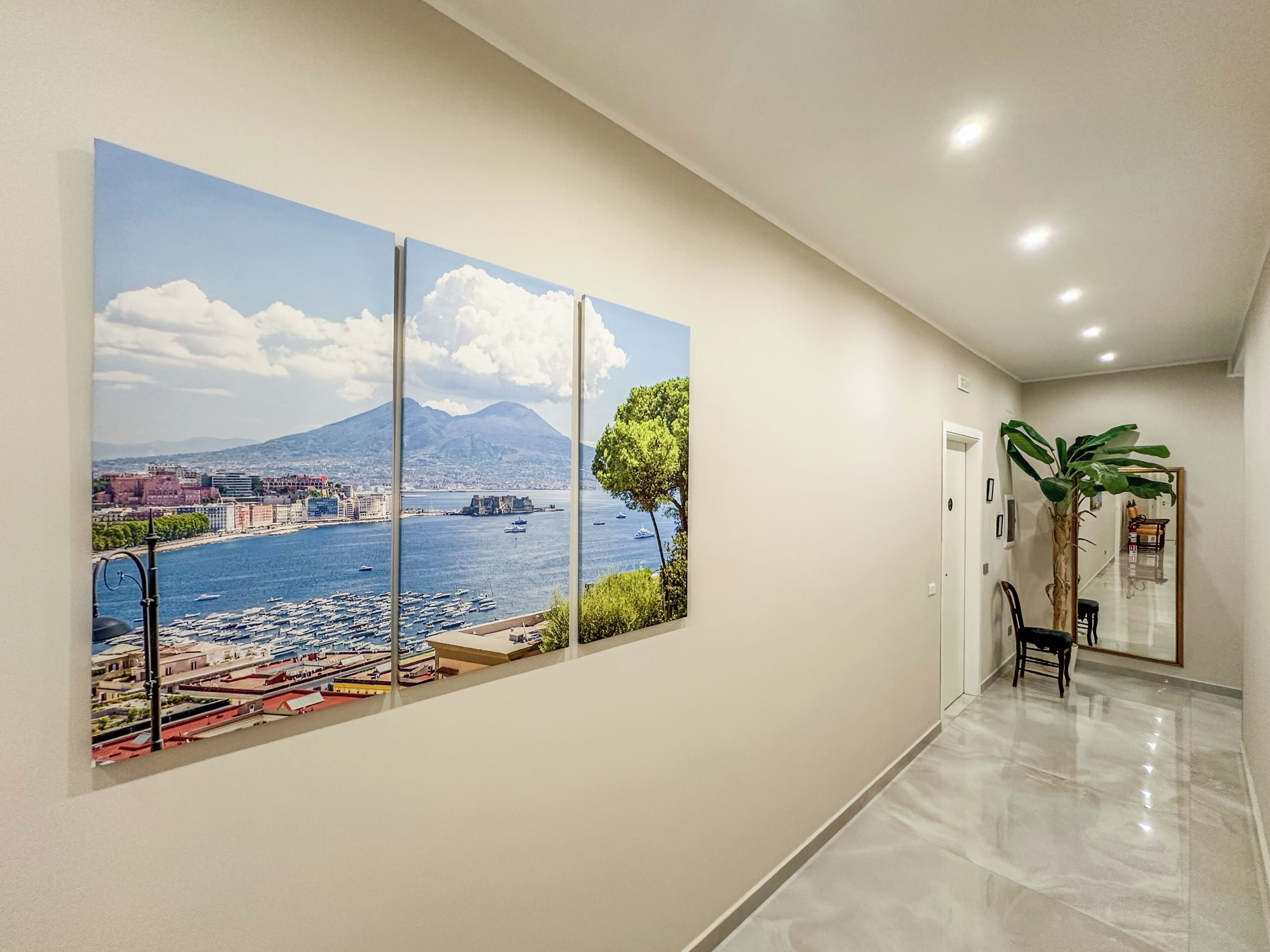 A hallway with a large landscape painting, a potted plant, and a chair.