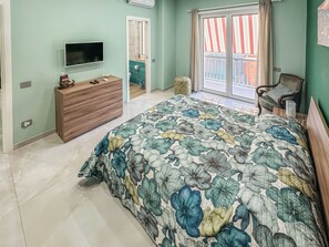A bedroom with a large bed, a wooden dresser, a television, and a window with curtains. - Karim's House (Portici)