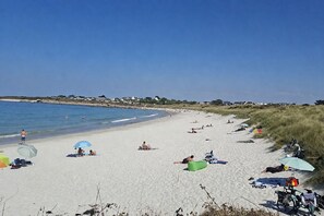 A beach with people sunbathing and swimming, a bicycle parked, and a grassy dune area. - House for 4, Jacuzzi & Garden, Beach 200 m Away (Plouguerneau)