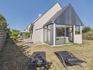 A modern house with a large glass door, a deck, and two lounge chairs. - House for 4, Jacuzzi & Garden, Beach 200 m Away (Plouguerneau)