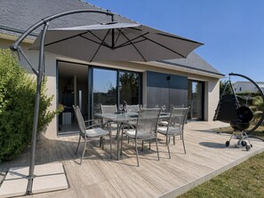 Une terrasse extérieure avec une table et des chaises, un grand parasol et un barbecue.