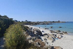Une plage avec un terrain rocheux, un ciel dégagé et quelques personnes.
