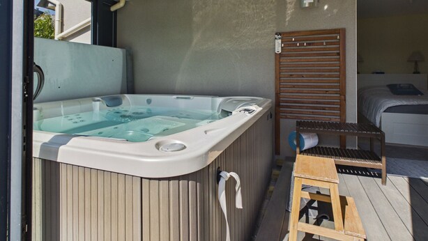 Un jacuzzi con muelle de madera y escalera, un banco de madera y una cama al fondo.
