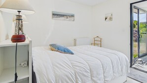 Un dormitorio con cama, lámpara, radiador y vistas a través de un ventanal.