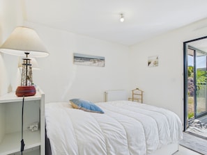 A bedroom with a bed, a lamp, a radiator, and a view through a glass door. - House for 4, Jacuzzi & Garden, Beach 200 m Away (Plouguerneau)