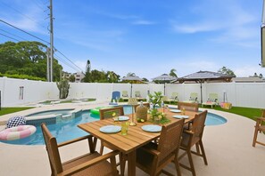 An outdoor pool area with a wooden table and chairs, surrounded by a white fence. - Pickleball, Hot Tub, Pool, Mini Golf, Arcades, Billiards, and More! (St. Petersburg)