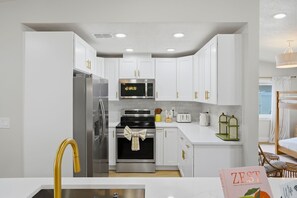 A modern kitchen with white cabinets, stainless steel appliances, and a yellow faucet. - Pickleball, Hot Tub, Pool, Mini Golf, Arcades, Billiards, and More! (St. Petersburg)