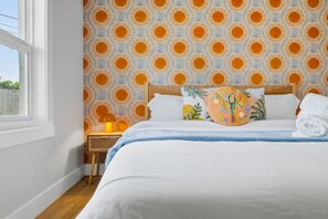 A hotel room with a large bed, a wooden headboard, a patterned wall, a small table with a lamp, and a window. - Pickleball, Hot Tub, Pool, Mini Golf, Arcades, Billiards, and More! (St. Petersburg)
