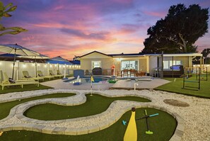 A modern outdoor pool area with lounge chairs, a children's play area, and a building with large windows. - Pickleball, Hot Tub, Pool, Mini Golf, Arcades, Billiards, and More! (St. Petersburg)