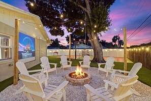 An outdoor seating area with Adirondack chairs around a fire pit, a Disney-themed sign, and string lights. - Pickleball, Hot Tub, Pool, Mini Golf, Arcades, Billiards, and More! (St. Petersburg)