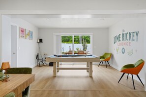 A modern room with a pool table, green chairs, and a view of greenery outside. - Pickleball, Hot Tub, Pool, Mini Golf, Arcades, Billiards, and More! (St. Petersburg)