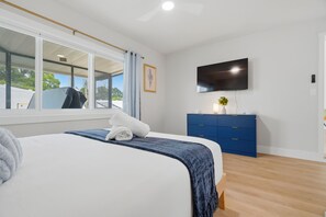 A bedroom with a bed, a TV, a blue cabinet, and a window with a view of the outside. - Pickleball, Hot Tub, Pool, Mini Golf, Arcades, Billiards, and More! (St. Petersburg)