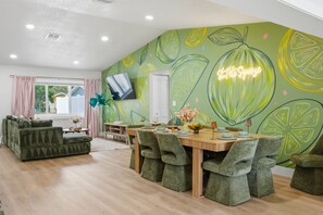 A dining area with a green leaf-patterned wall, a flat-screen TV mounted above the table, and a neon sign reading 'St. Pete Squeeze'. - Pickleball, Hot Tub, Pool, Mini Golf, Arcades, Billiards, and More! (St. Petersburg)
