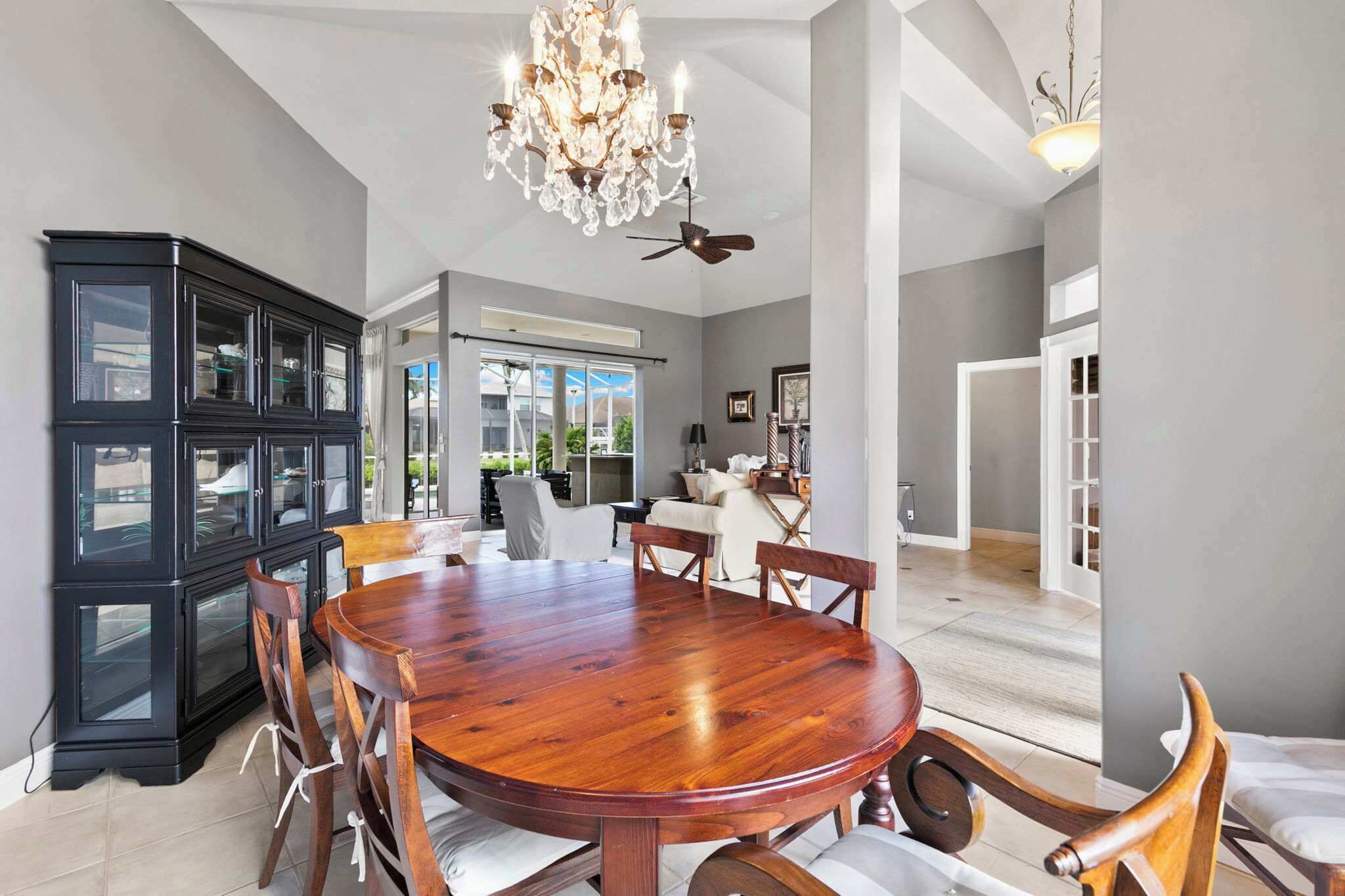 A spacious dining area with a large wooden table surrounded by chairs, a black cabinet with glass doors, and a chandelier.