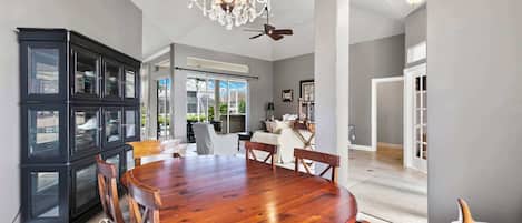 A spacious dining area with a large wooden table surrounded by chairs, a black cabinet with glass doors, and a chandelier.