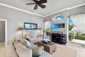 A living room with a sofa, a coffee table, a TV, and a ceiling fan. - Waterfront Retreat - Private Pool - Large Dock (Marco Island)