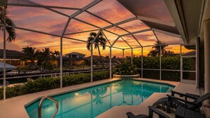 Piscina com vista para palmeiras e um pôr do sol.