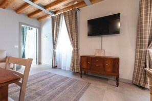 A room with a wooden ceiling, a flat-screen TV mounted on the wall, a wooden cabinet with drawers, a patterned rug, and a door with curtains.
