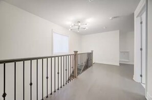 A clean, modern hallway with a wooden railing and a ceiling light fixture. - Cozy 5BR Haven• Backyard • Pet Friendly • Parking (Richmond Hill)