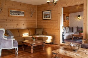 A cozy room with wooden walls, a sofa, a chair, a coffee table, and a fireplace. - Huge amazing chalet with 13 bedrooms, private garden and en-suites (Vaujany)