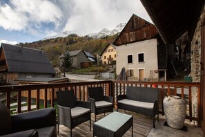Eine Holzterrasse mit Korbmöbeln, einem Steinvase und Blick auf ein Gebirge.