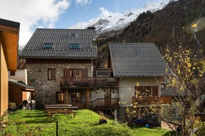 Ein zweigeschossiges Steinhaus mit Balkon, einer Holzterrasse und Bergblick.