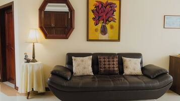Uma sala de estar com um sofá de couro escuro, um espelho redondo, uma mesa com abajur e um quadro na parede.
