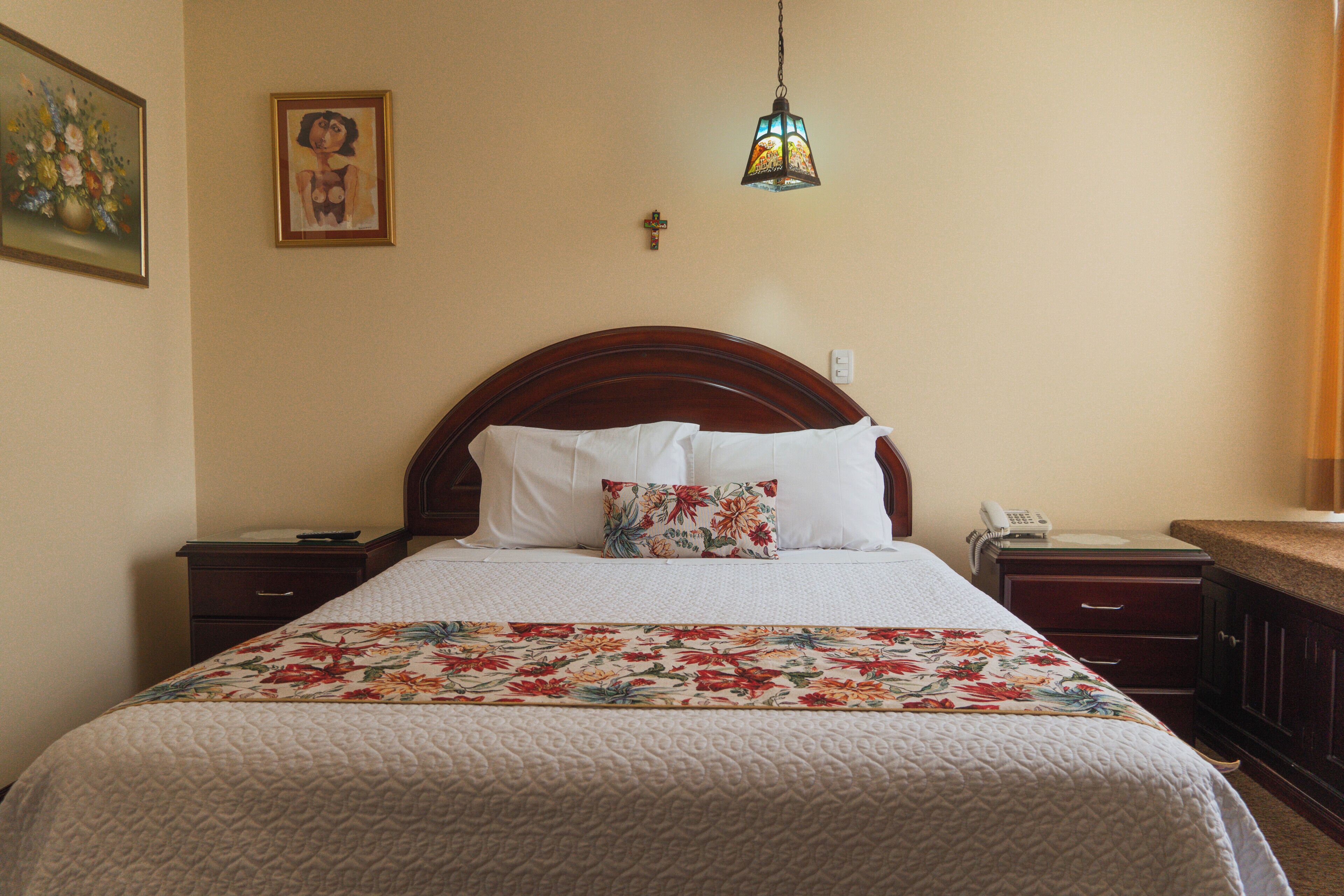 Una habitación de hotel con una cama grande, una mesita de noche, un teléfono y una lámpara colgante.