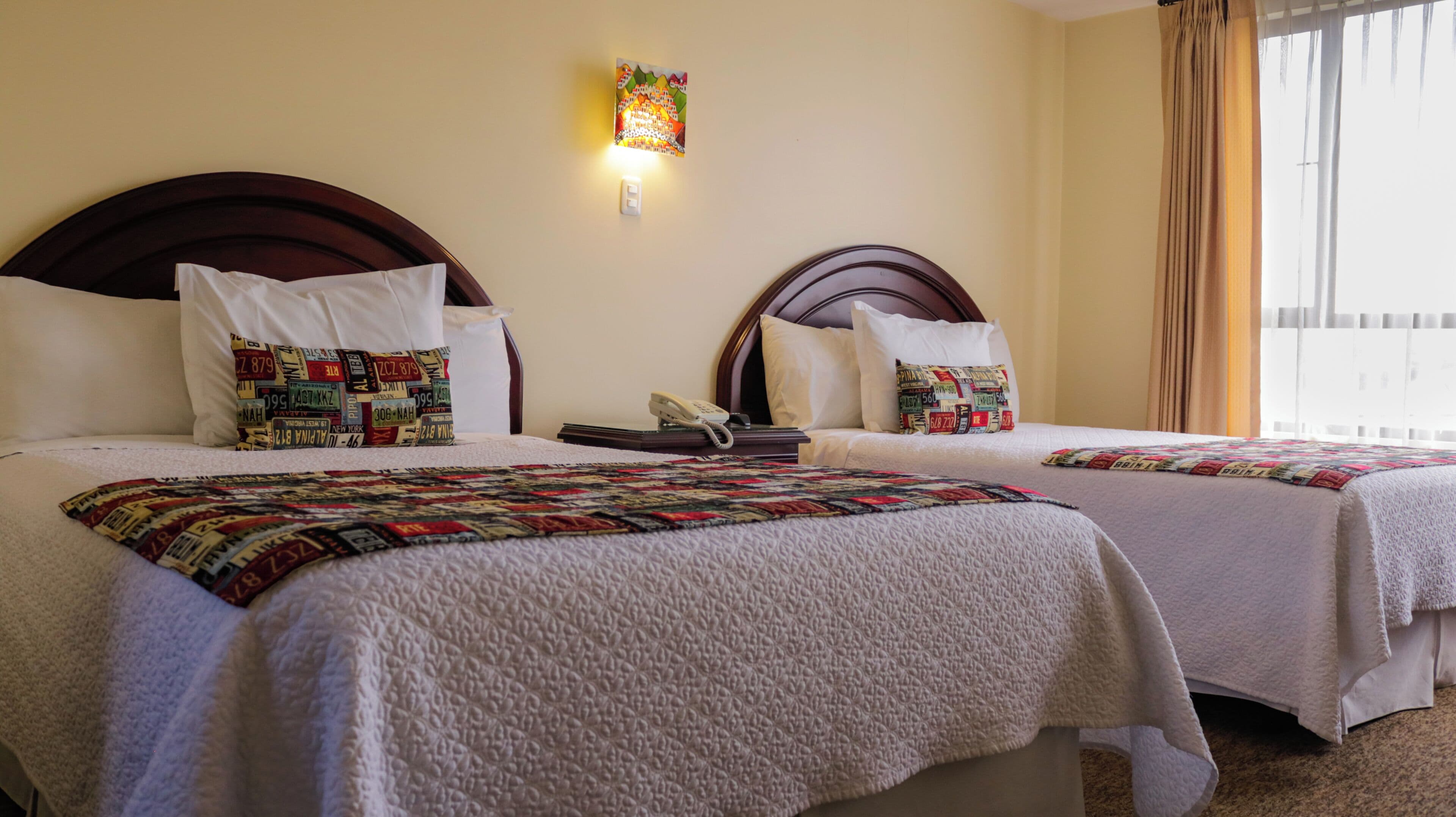 Habitación de hotel con dos camas, cada una con una colcha estampada, teléfono en la mesita de noche y una lámpara fijada a la pared.
