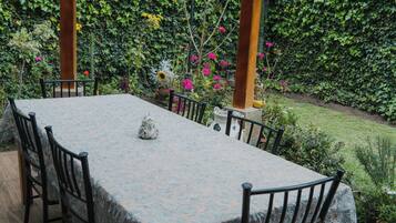 Alpendre coberto com mesa e cadeiras, cercado por vegetação e um jardim.