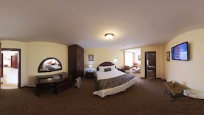 Une chambre d’hôtel avec un grand lit, une commode, un miroir, une télévision et une porte donnant sur une autre pièce.