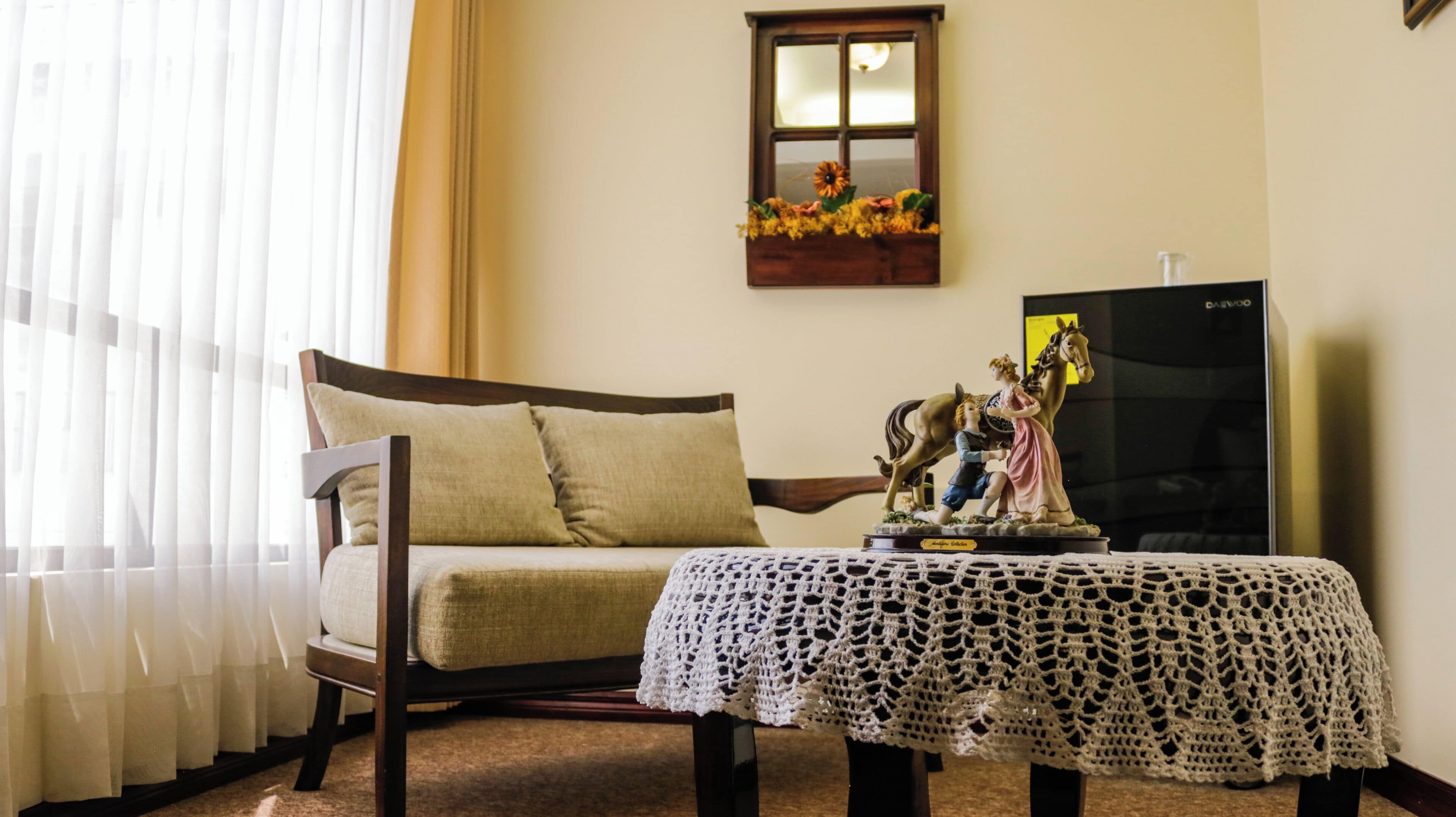 A room with a bed, a small table with a crocheted tablecloth, a statue, and a television.
