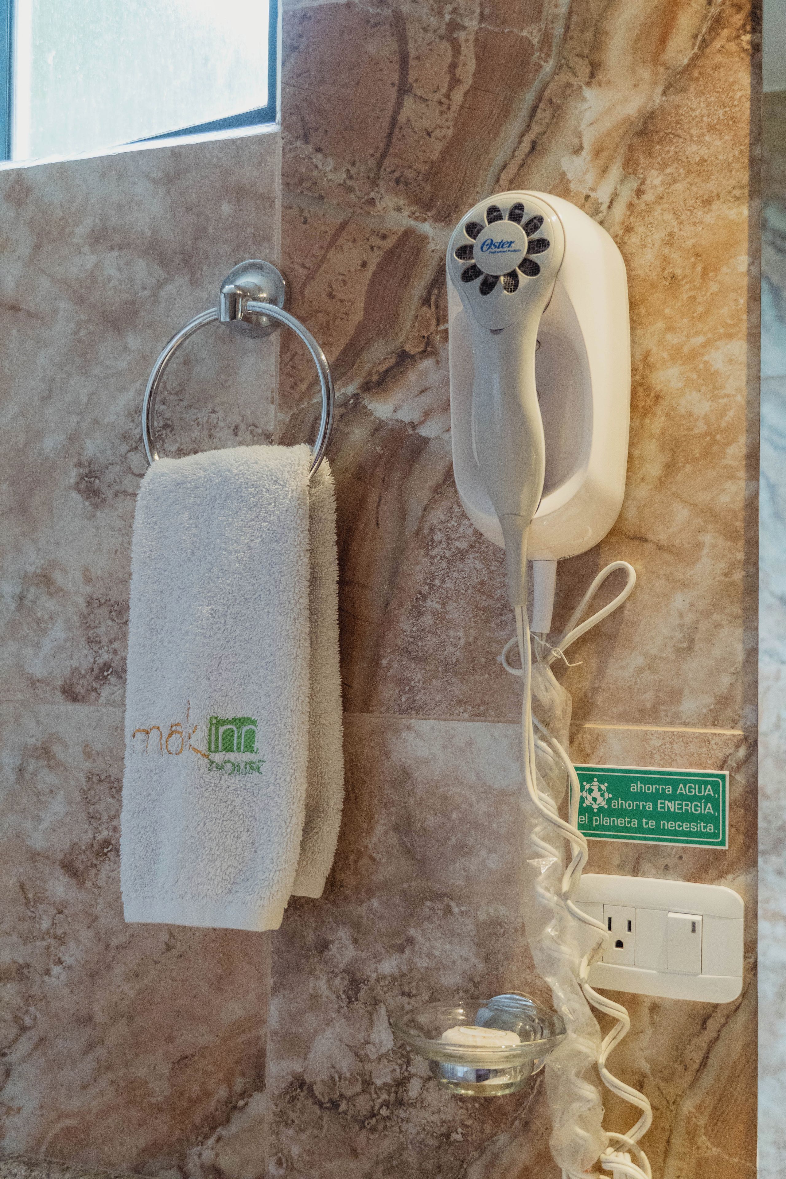 A towel hanging on a metal ring, a hairdryer, and a power outlet with a green sign.