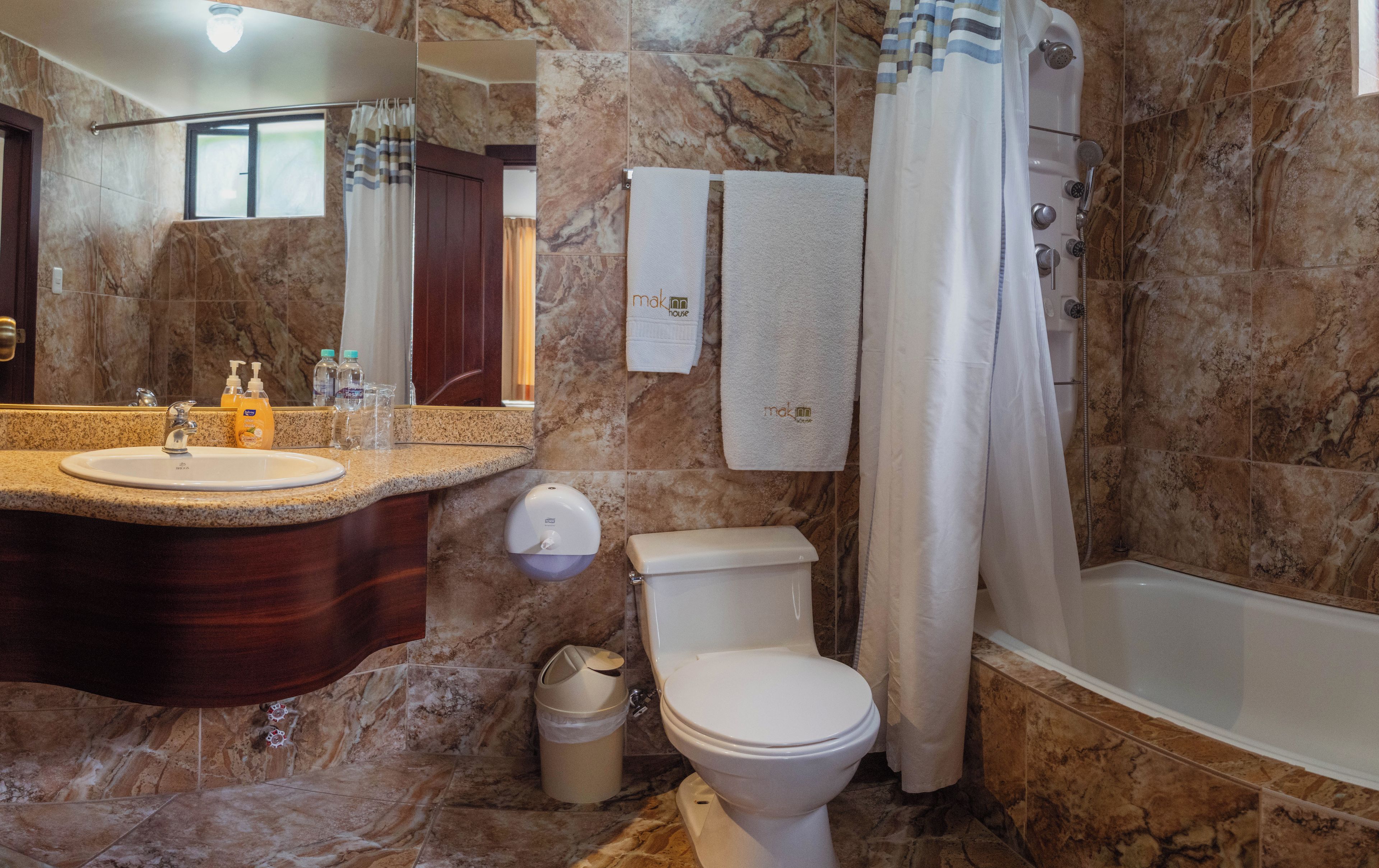 A bathroom with a marble wall, a sink with a mirror, a toilet, and a shower with a curtain.