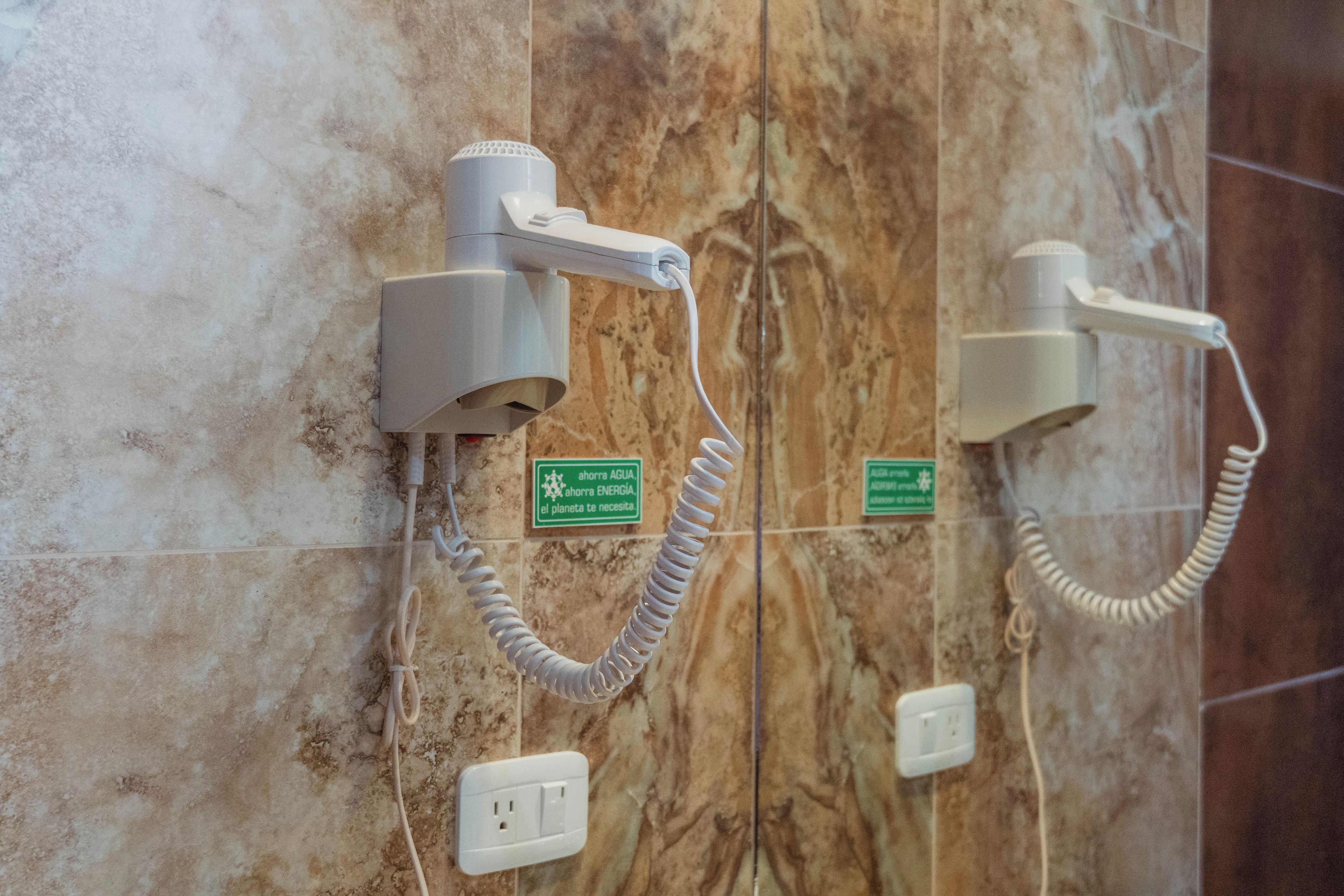 Two hair dryers mounted on a marble wall with a coiled cord and a power outlet below.