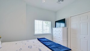 Un dormitorio con una cama, un aparador, un televisor encima y una ventana con persianas.
