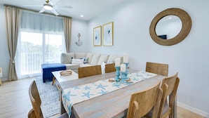 Comedor con mesa lista para cuatro personas, ventilador de techo y vistas al exterior a través de amplios ventanales.