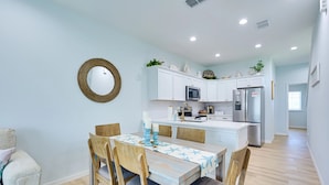 Una cocina moderna con armarios blancos, un refrigerador de acero inoxidable y una zona de comedor con mesa y sillas.
