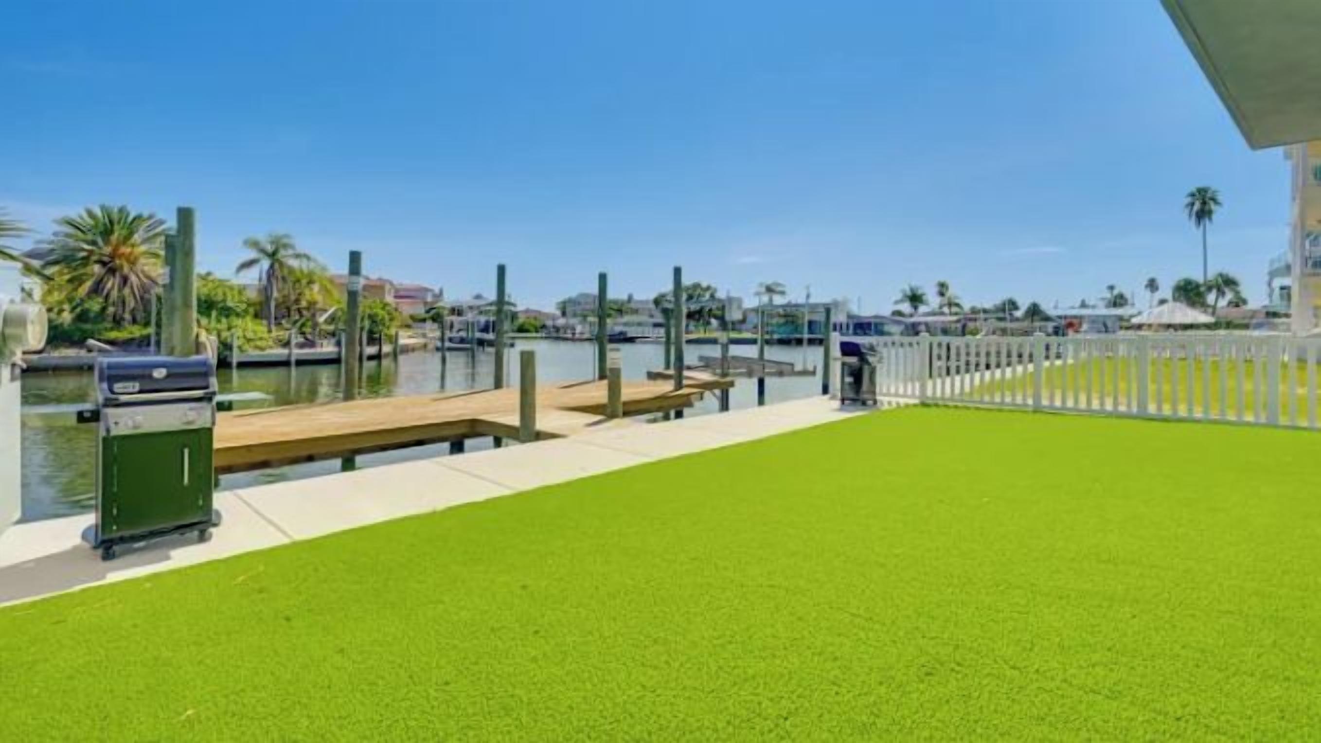Un puerto deportivo con césped, un muelle de madera y una parrilla.