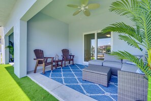 A balcony with a ceiling fan, two wooden chairs, a small table with a lantern, a grey sofa, and a large potted plant. - Steps to Dock & Sand! Waterfront Hudson Retreat (Hudson)